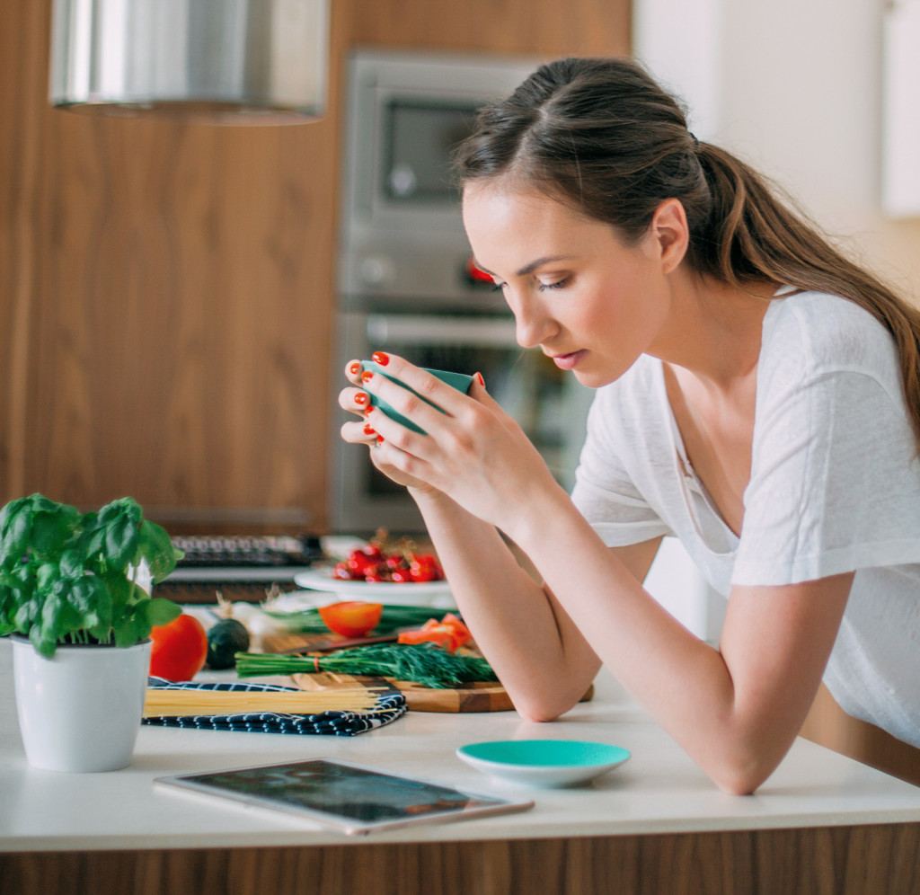 Person holding cup and looking at a tablet on the kitchen